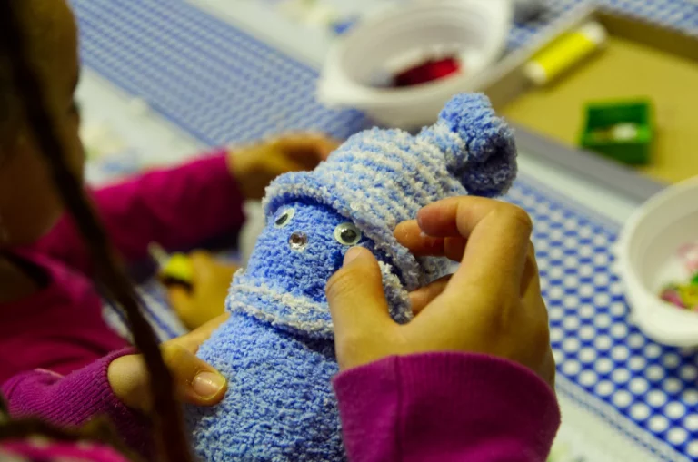 Kind mit Zöpfen bastelt einen blauen Schneemann mit Mütze aus Wolle